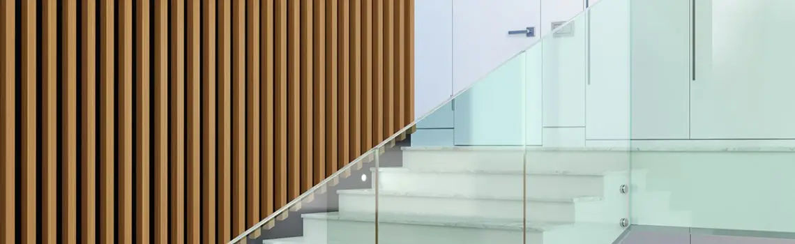 KP Glazing London A modern staircase with white steps and a glass balustrade is next to a wall featuring vertical wooden slats in a contemporary interior space.