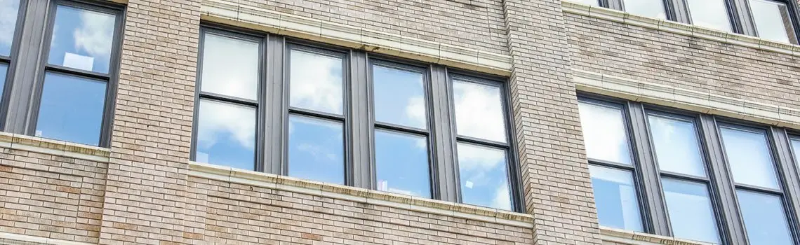 KP Glazing London A close-up view of a brick building façade with large rectangular windows reflecting blue sky and clouds.