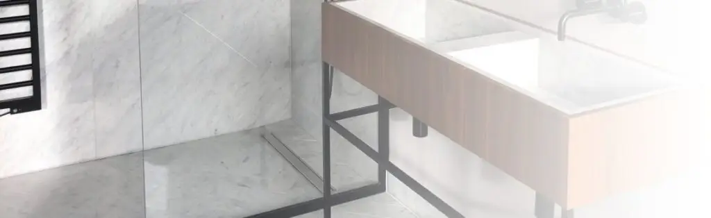 KP Glazing London Modern bathroom with marble floors and walls, a wooden vanity with a white basin, black tap, and black metal legs. There is a walk-in shower with a glass panel and a black heated towel rail on the wall.
