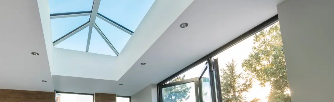 KP Glazing London Modern interior with a large glass roof lantern and open folding doors, allowing natural light to fill the space. Trees and sunlight are visible outside through the open doors.