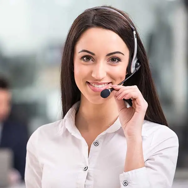 KP Glazing London A woman wearing a white shirt and a headset smiles whilst holding the microphone, appearing to work in customer service or a call centre. The background is blurred.