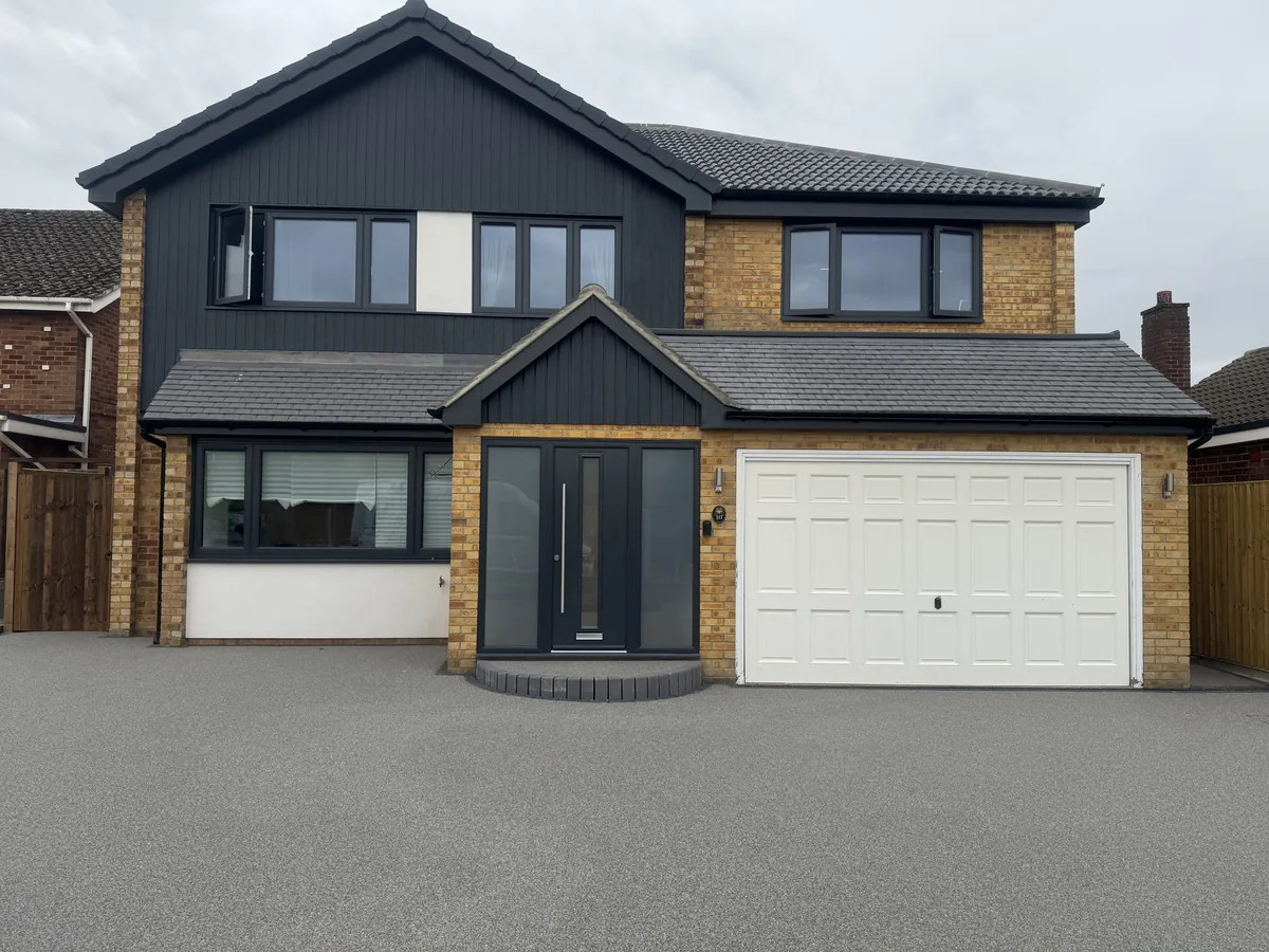 KP Glazing London Modern two-storey house with brick and dark grey cladding, large windows, a double front door, and a white garage door, set on a paved drive under a cloudy sky.