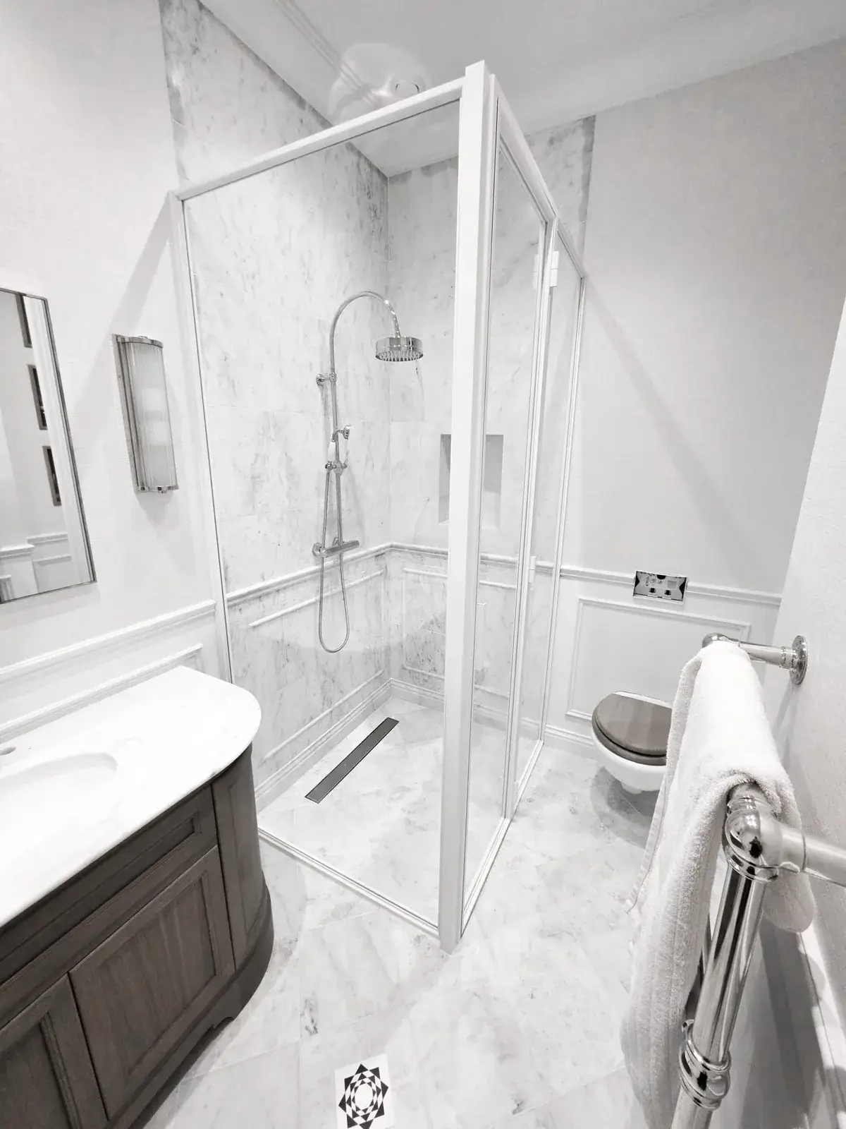 KP Glazing London A bathroom with a marble-tiled shower, a wooden vanity with a white worktop, and a wall-mounted toilet with a towel rail.