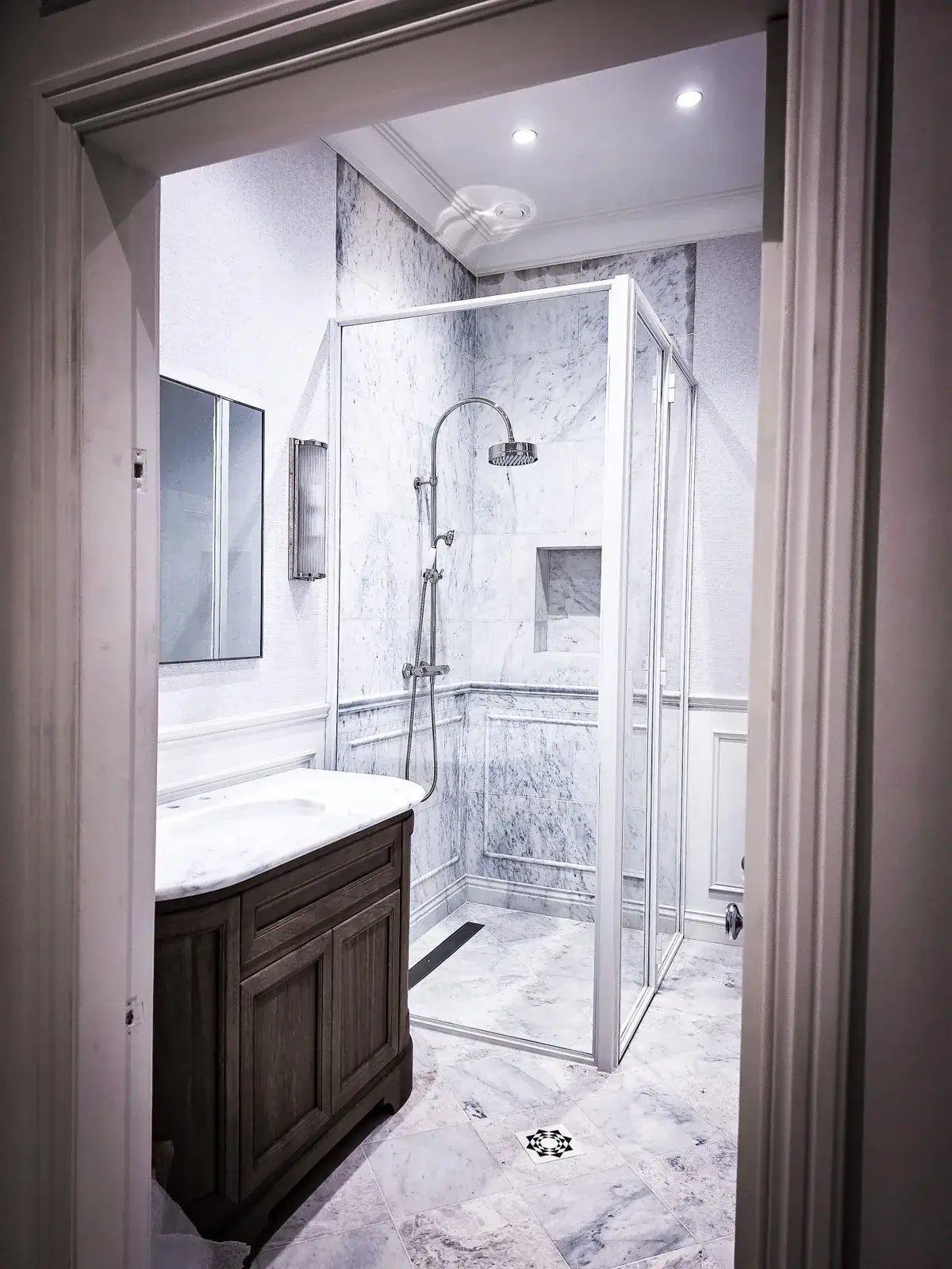 KP Glazing London A marble-tiled bathroom featuring a wooden vanity with a white countertop, a square glass-enclosed shower, and a rainfall shower head.