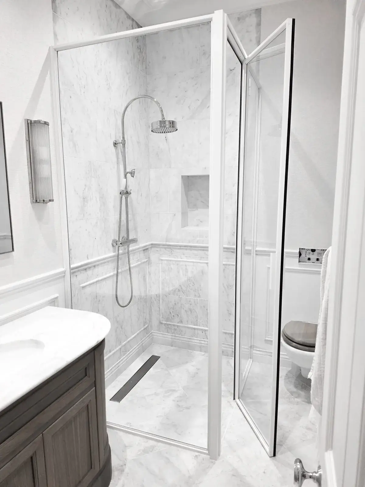 KP Glazing London Walk-in shower with a rain shower head and marble tiled walls, next to a marble-topped vanity unit and a toilet.